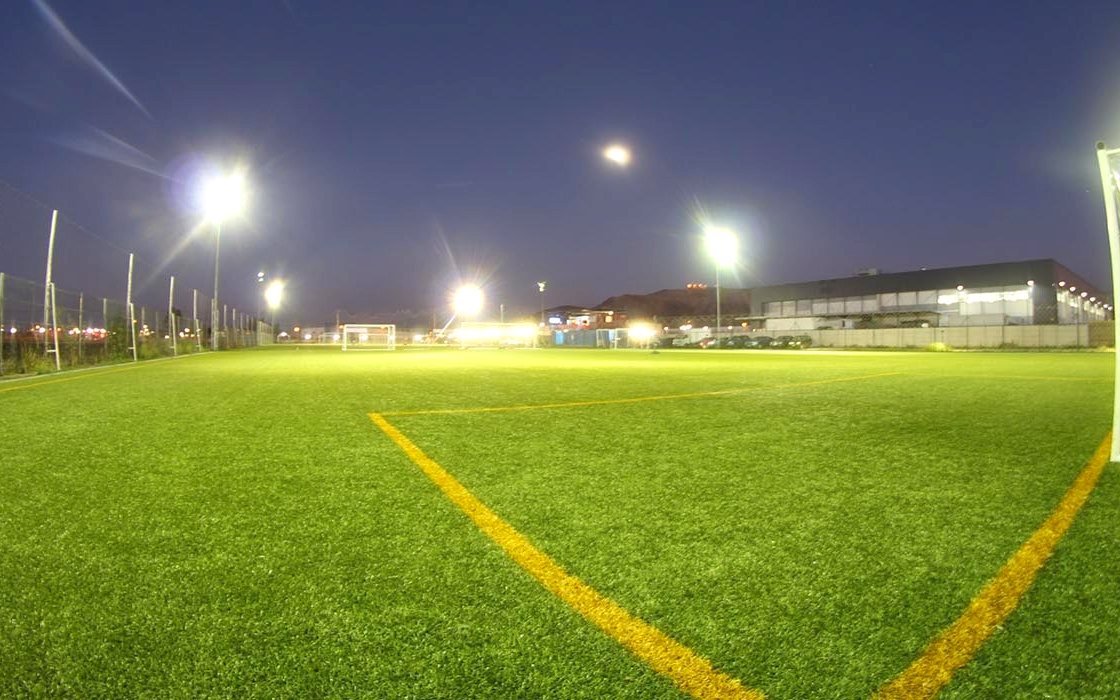 Cancha de futbolito iluminada de noche con las torres de luz encendidas