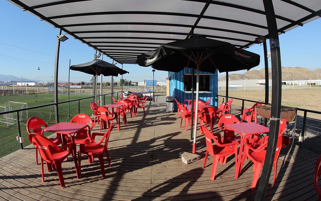 Terraza techada con mesas y sillas frente a las canchas